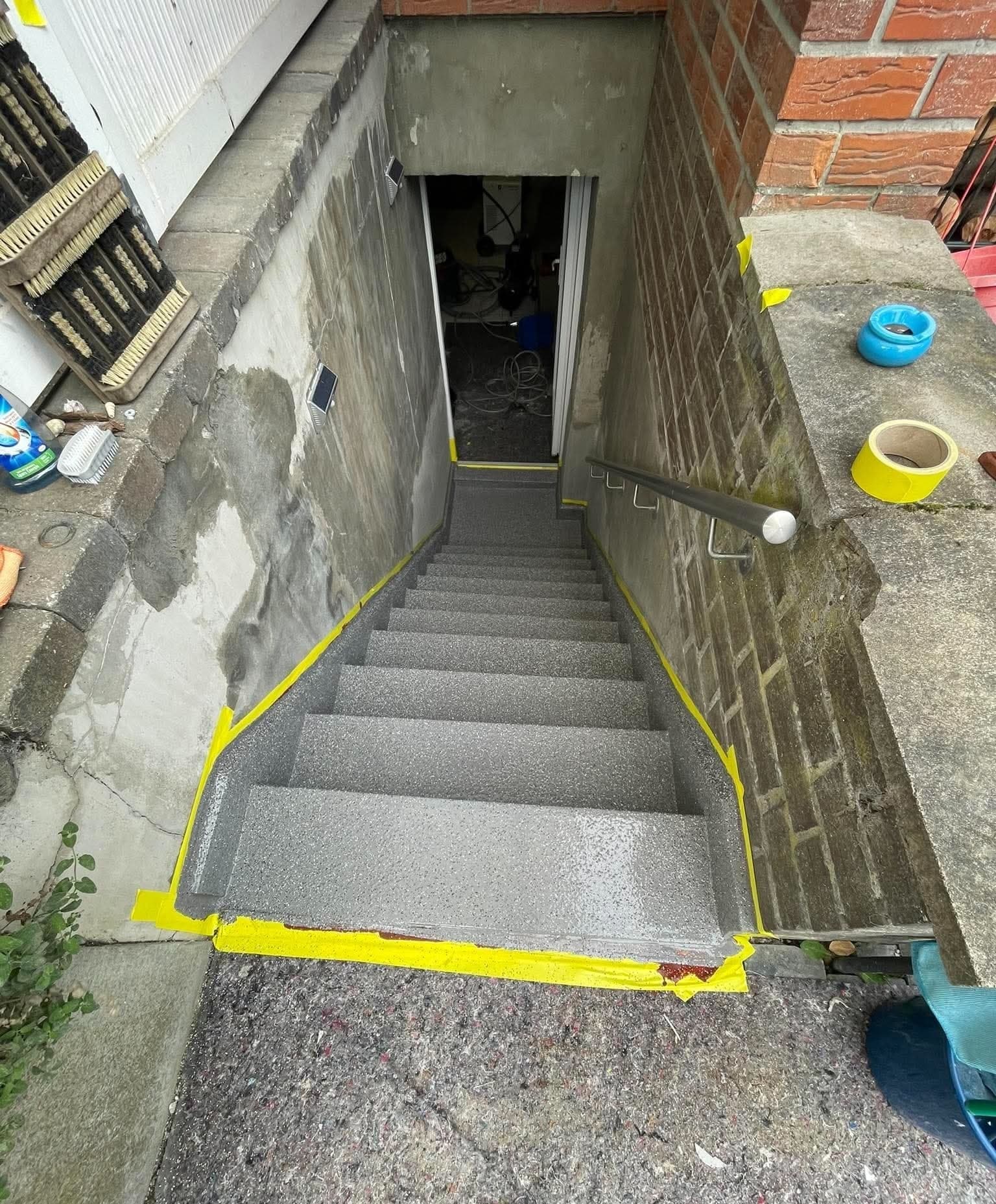 Kellerabgang von oben mit frisch aufgebrachter grauer Beschichtung, Ränder mit gelbem Klebeband abgeklebt