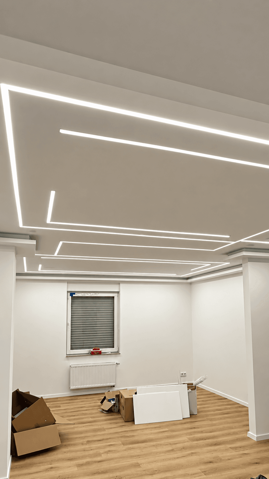 Fertig ausgebauter Raum mit abgehängter Decke, LED-Lichtlinien und Holzboden